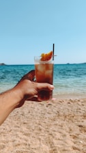 A person holding up a drink on a beach