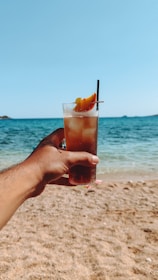 A person holding up a drink on a beach