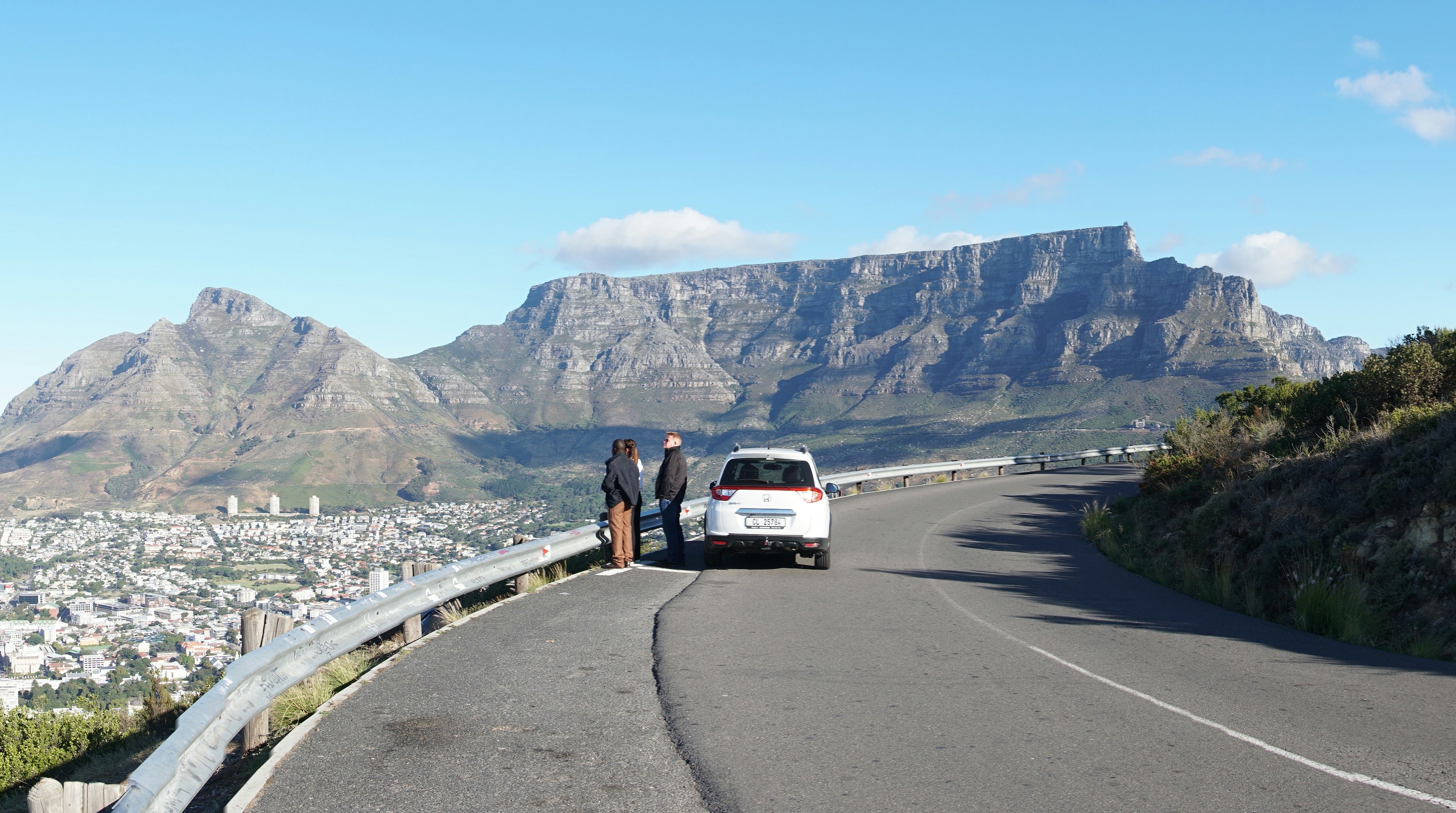 A white van driving down a curvy road next to a mountain