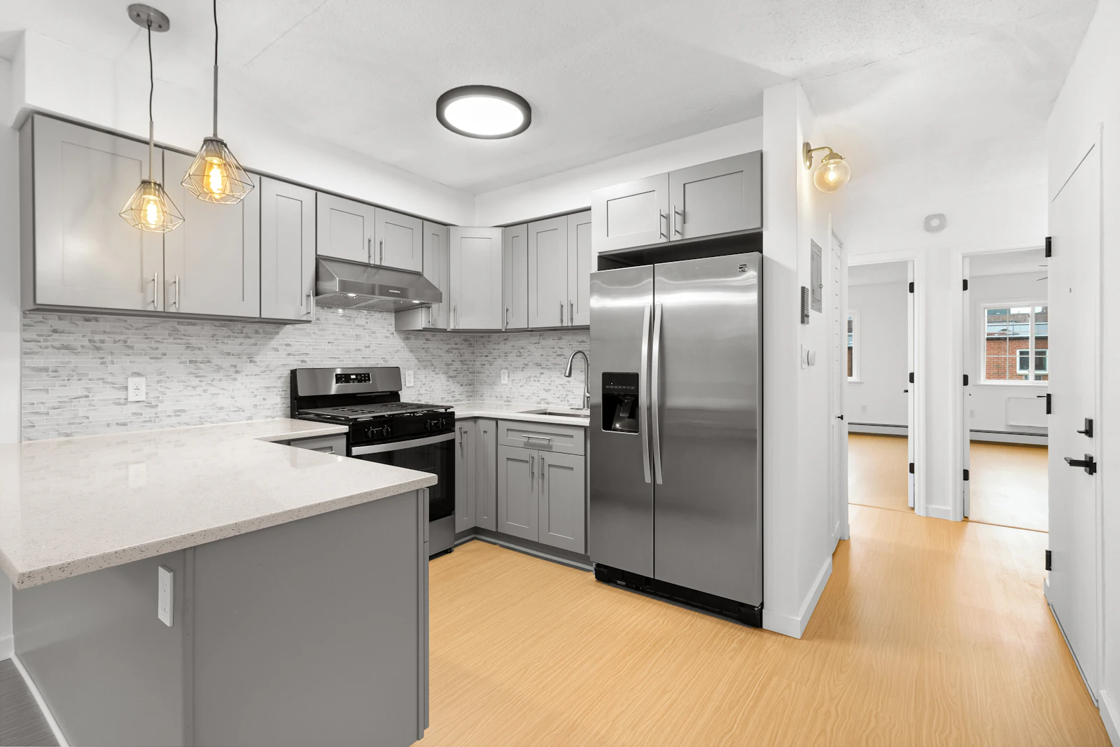 Modern kitchen with grey cabinetry, a stainless-steel refrigerator, gas stove, and light wood flooring