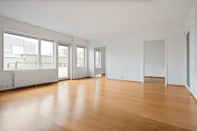An empty room with hard wood floors and windows