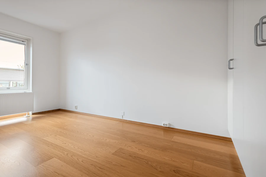 A cleared empty room with hardwood floors and a bright window after debris removal