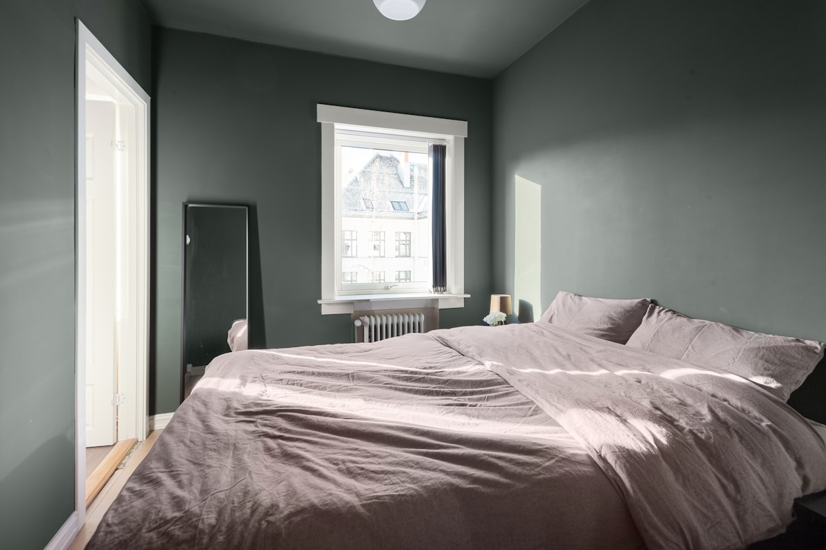 small bedroom with green accent walls and a leaning floor mirror, no headboard needed