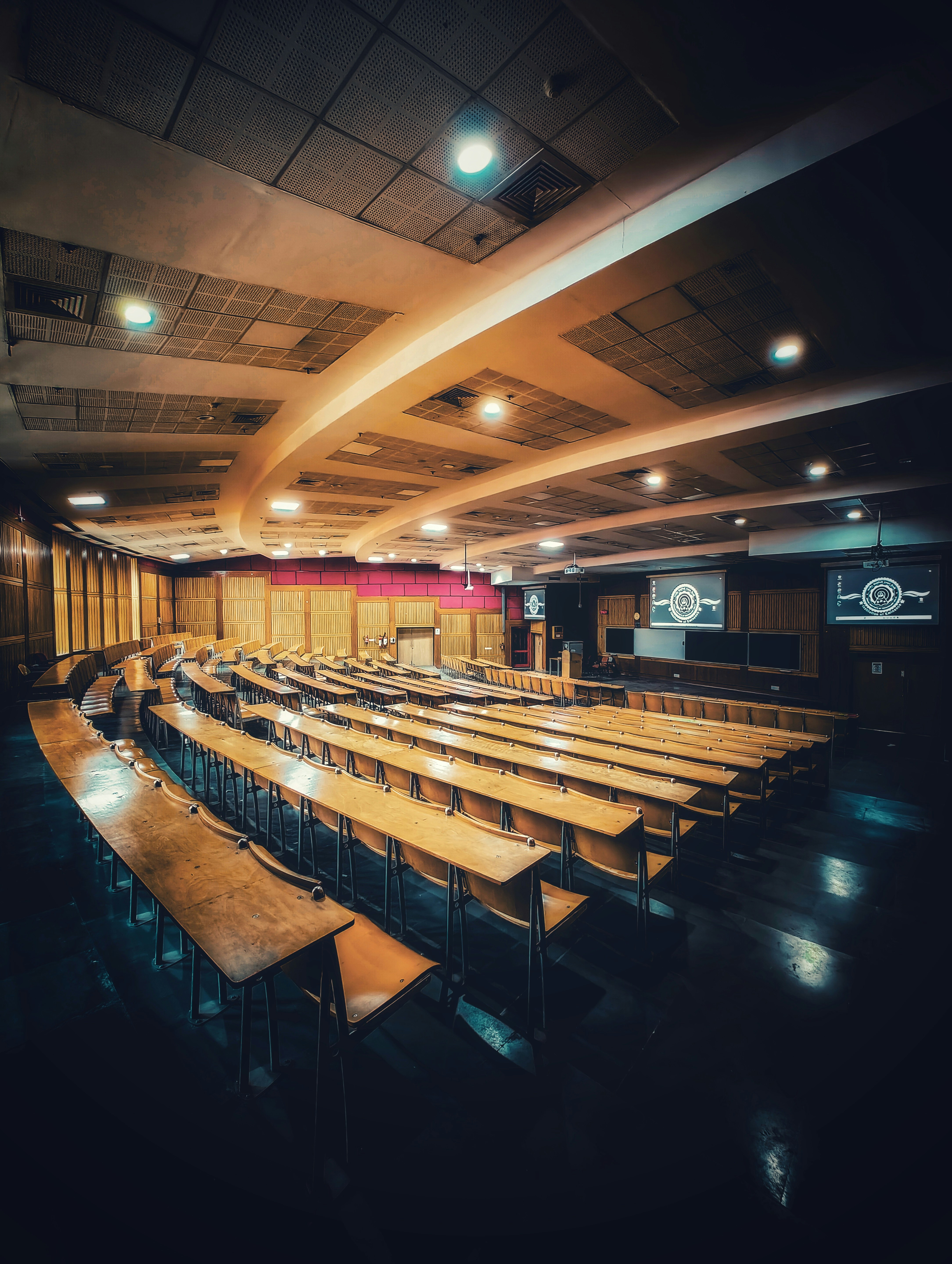 Empty lecture hall with rows of desks and projection screens.