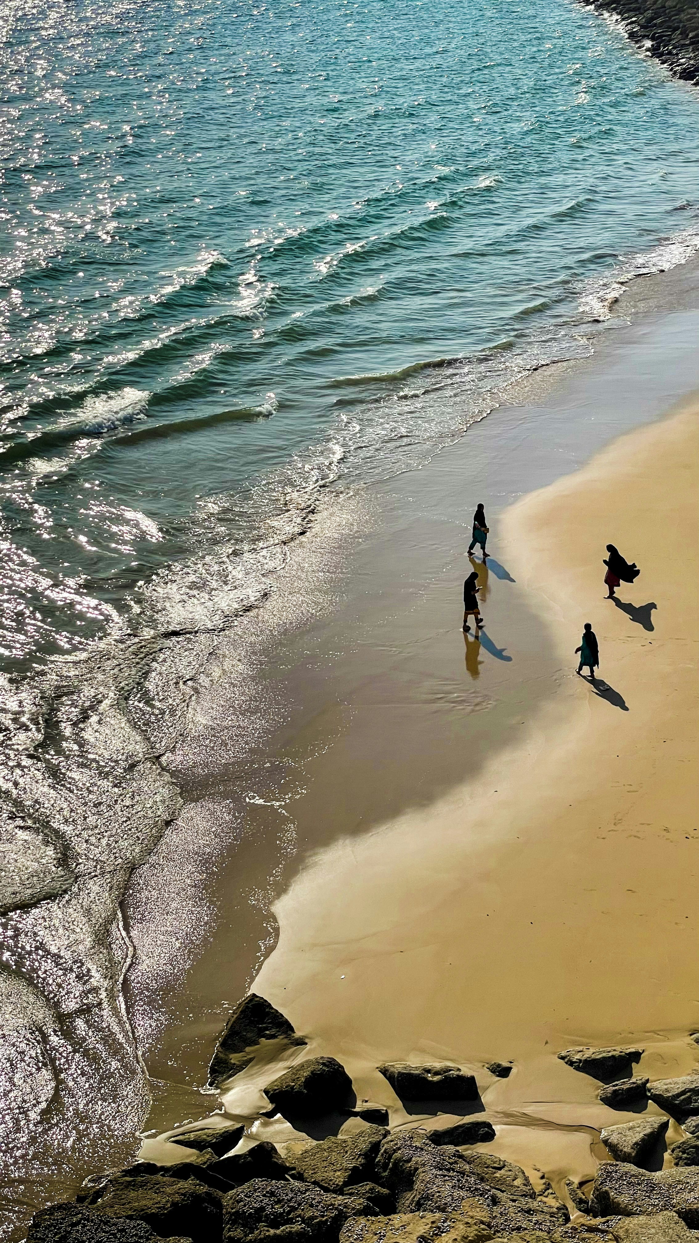 A group of people walking along a beach next to the ocean