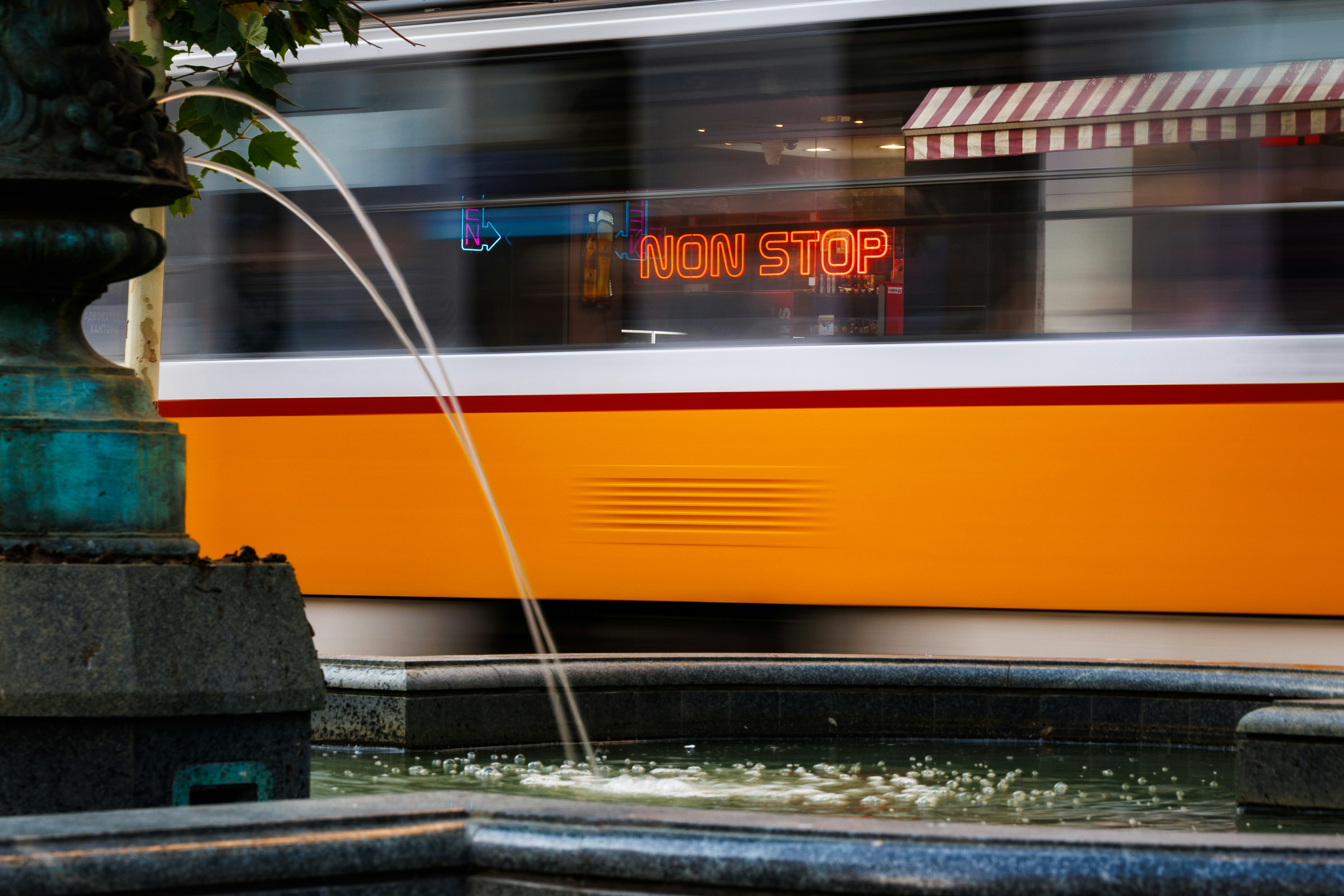 A yellow and white train passing by a fountain