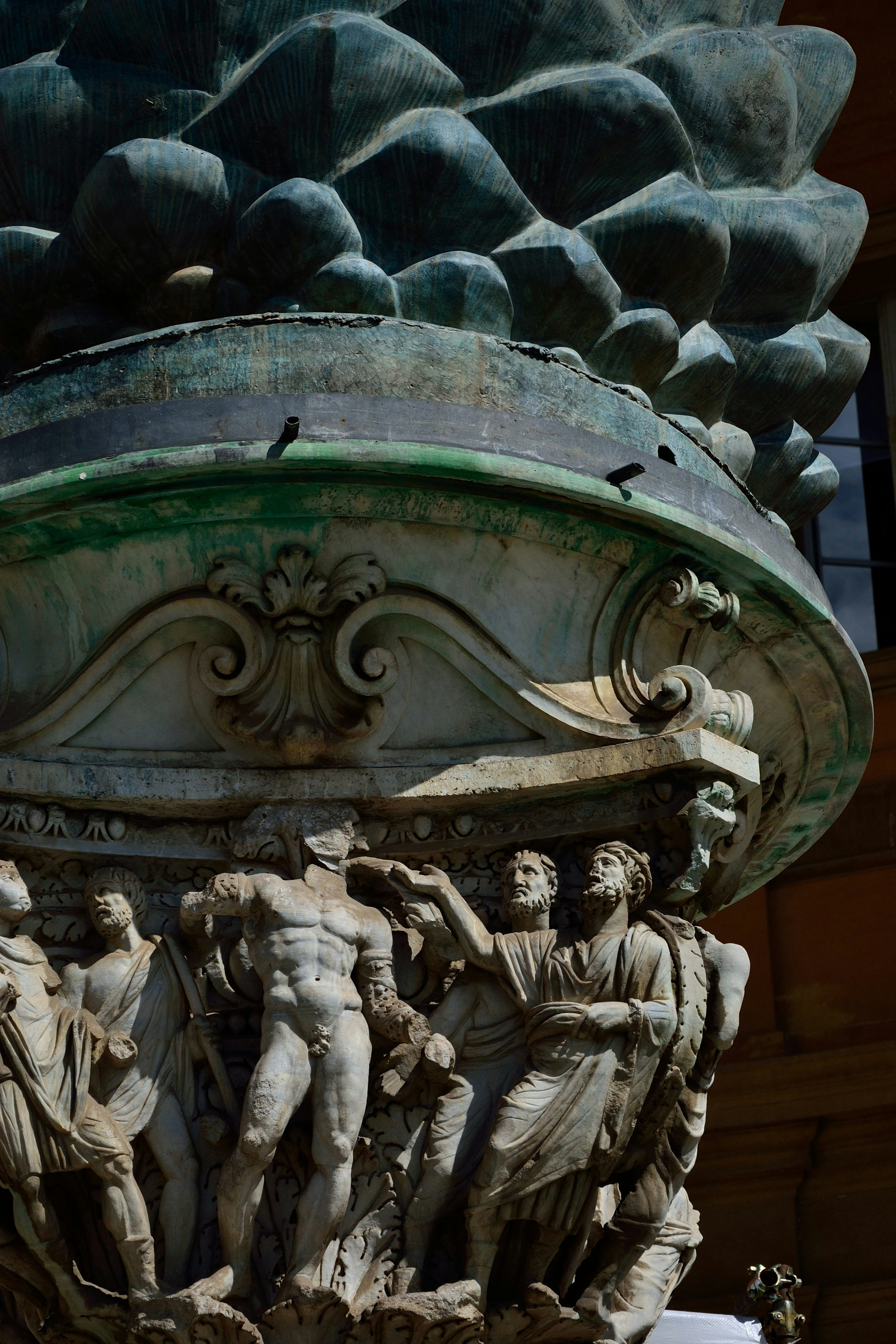 A close up of a statue with a pine cone in the background