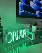 A desk with a computer monitor and a neon sign