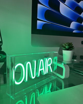 A desk with a computer monitor and a neon sign