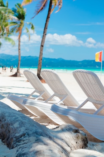 A row of white lawn chairs sitting on top of a sandy beach