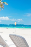 Two white lawn chairs sitting on top of a sandy beach