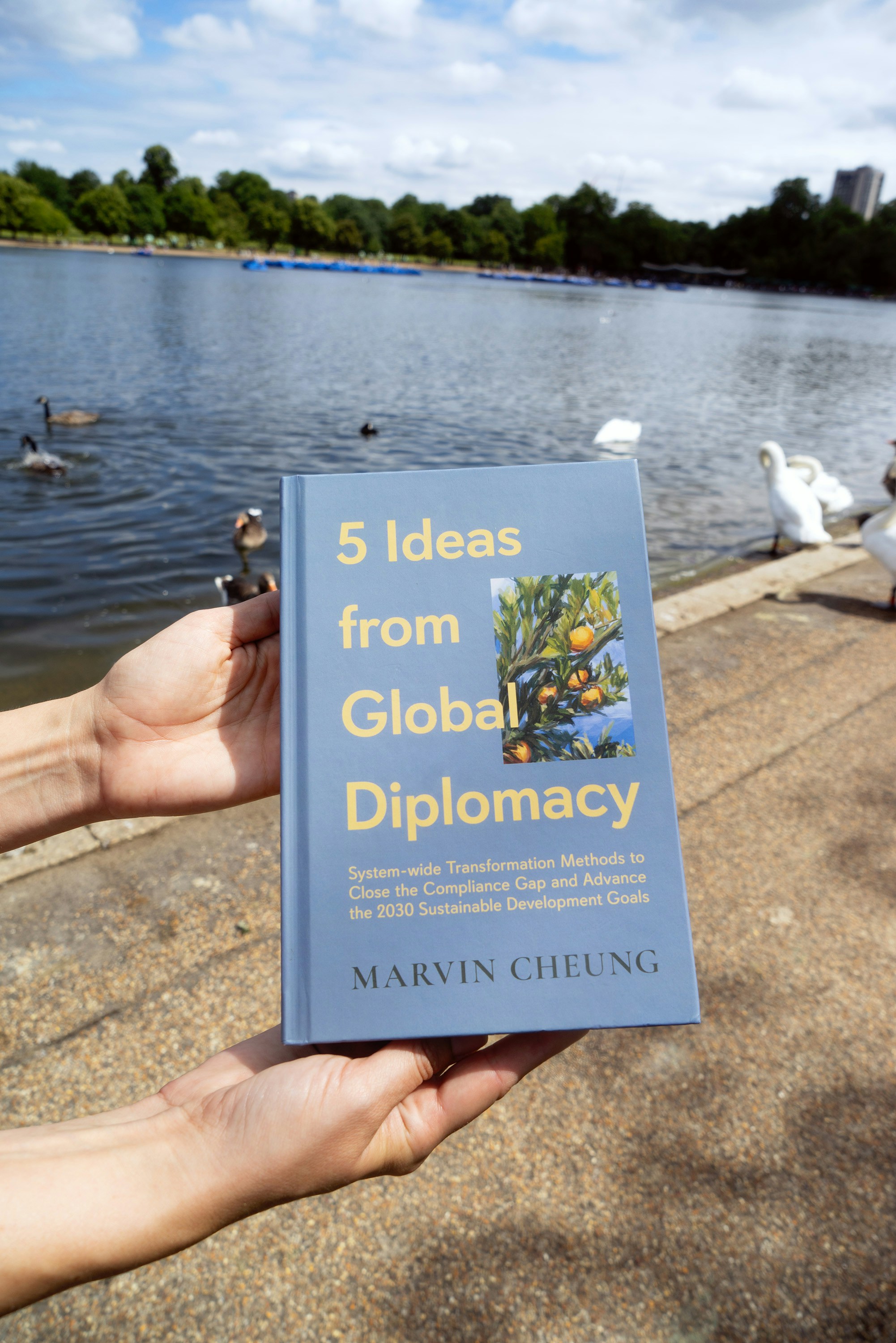 A person holding up a book in front of a lake