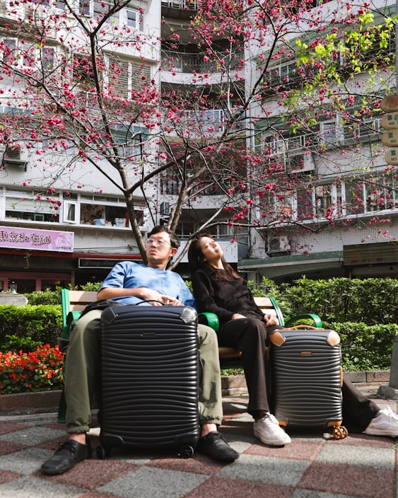 A man and woman sitting on a bench with their luggage