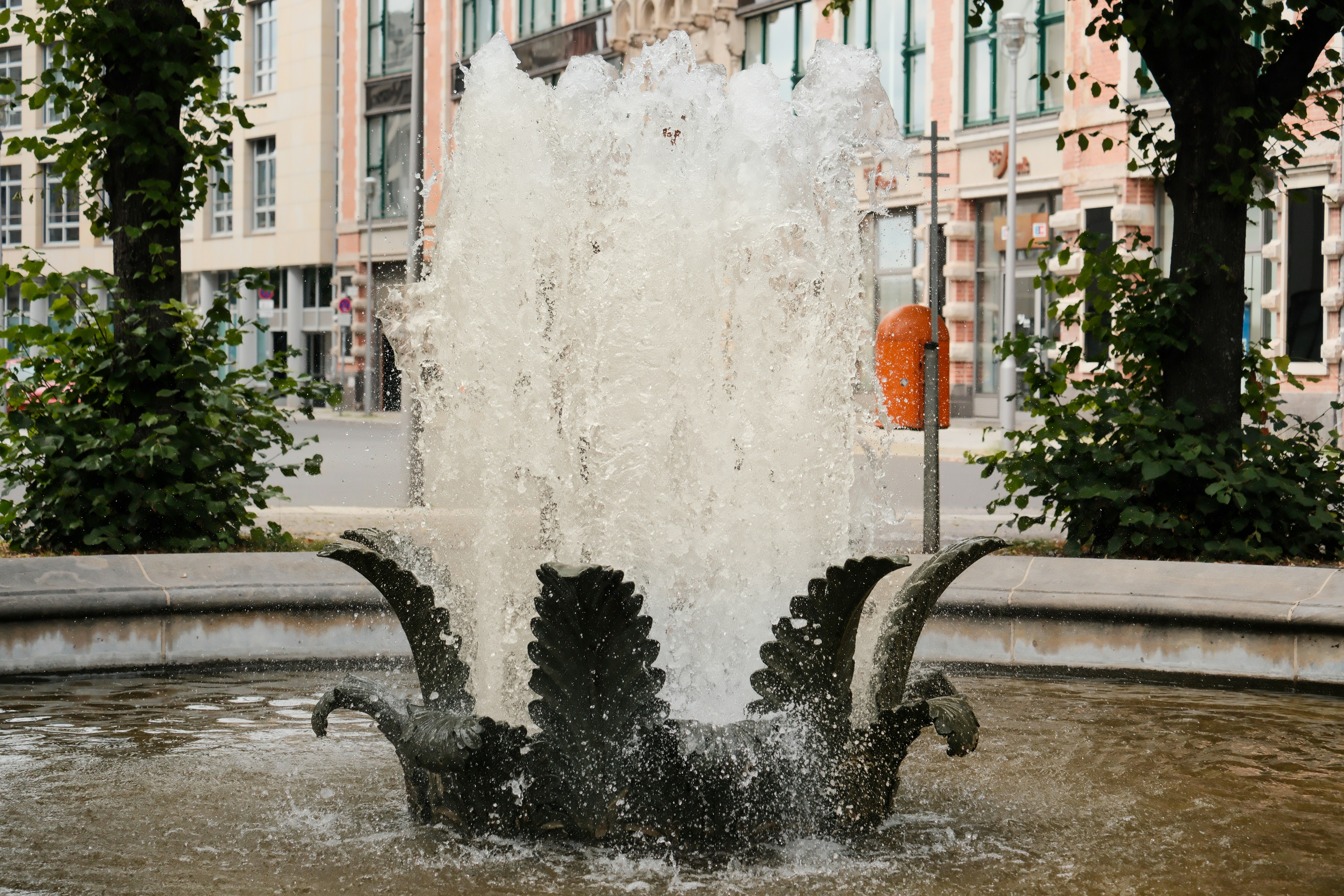 A water fountain in a city square with buildings in the background - a-water-fountain-in-a-city-square-with-buildings-in-the-background-WknXTePwzWk