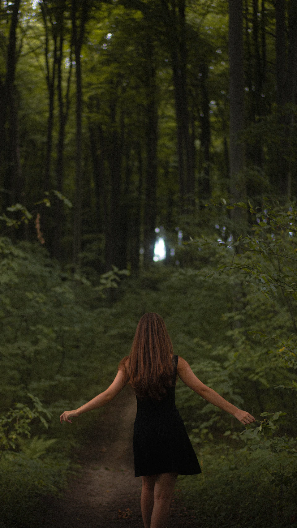 Young woman walking on a dirt path through a dense forest with tall trees above