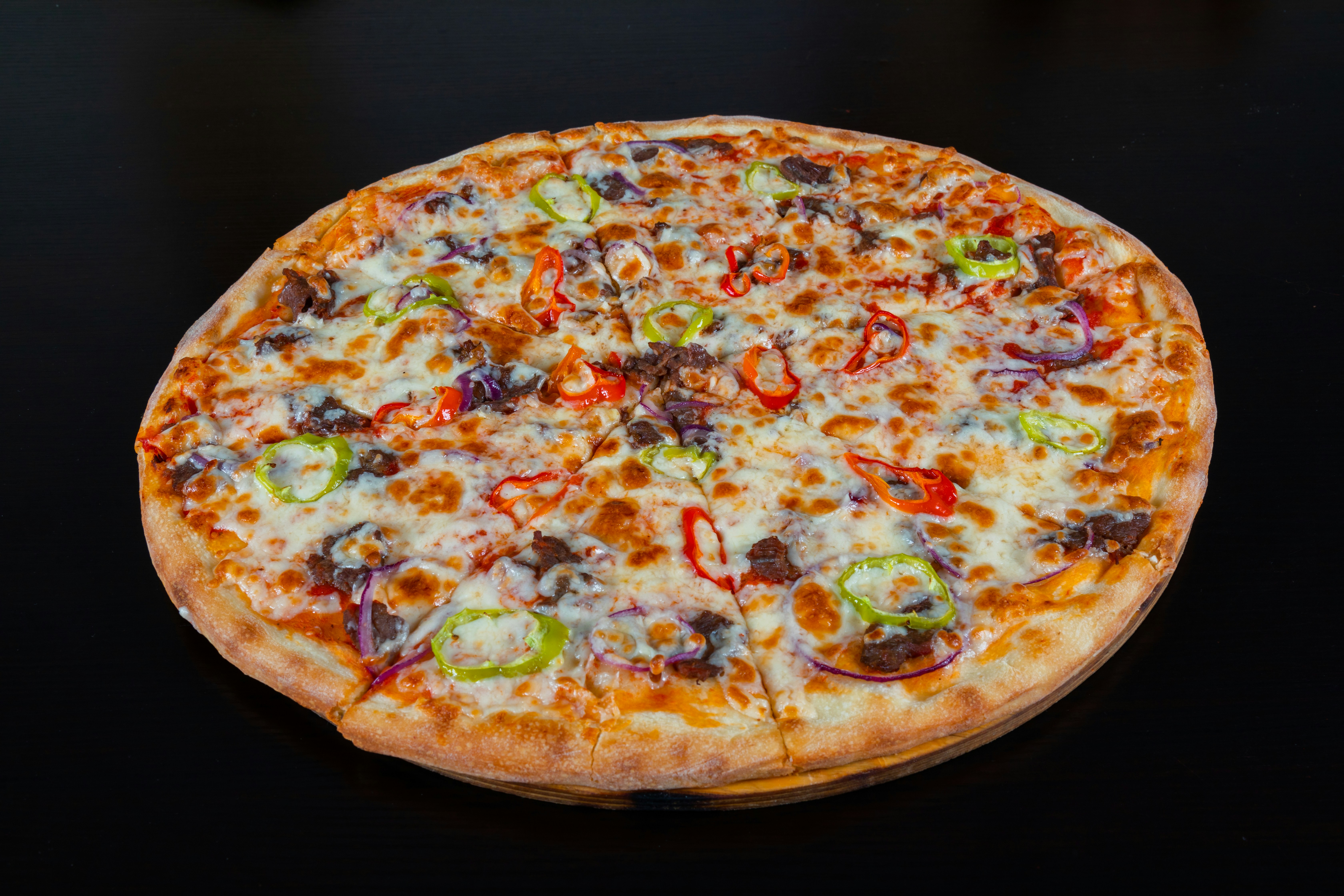 Loaded meat lover pizza with pepperoni, sausage, and beef, dark background with warm dramatic lighting