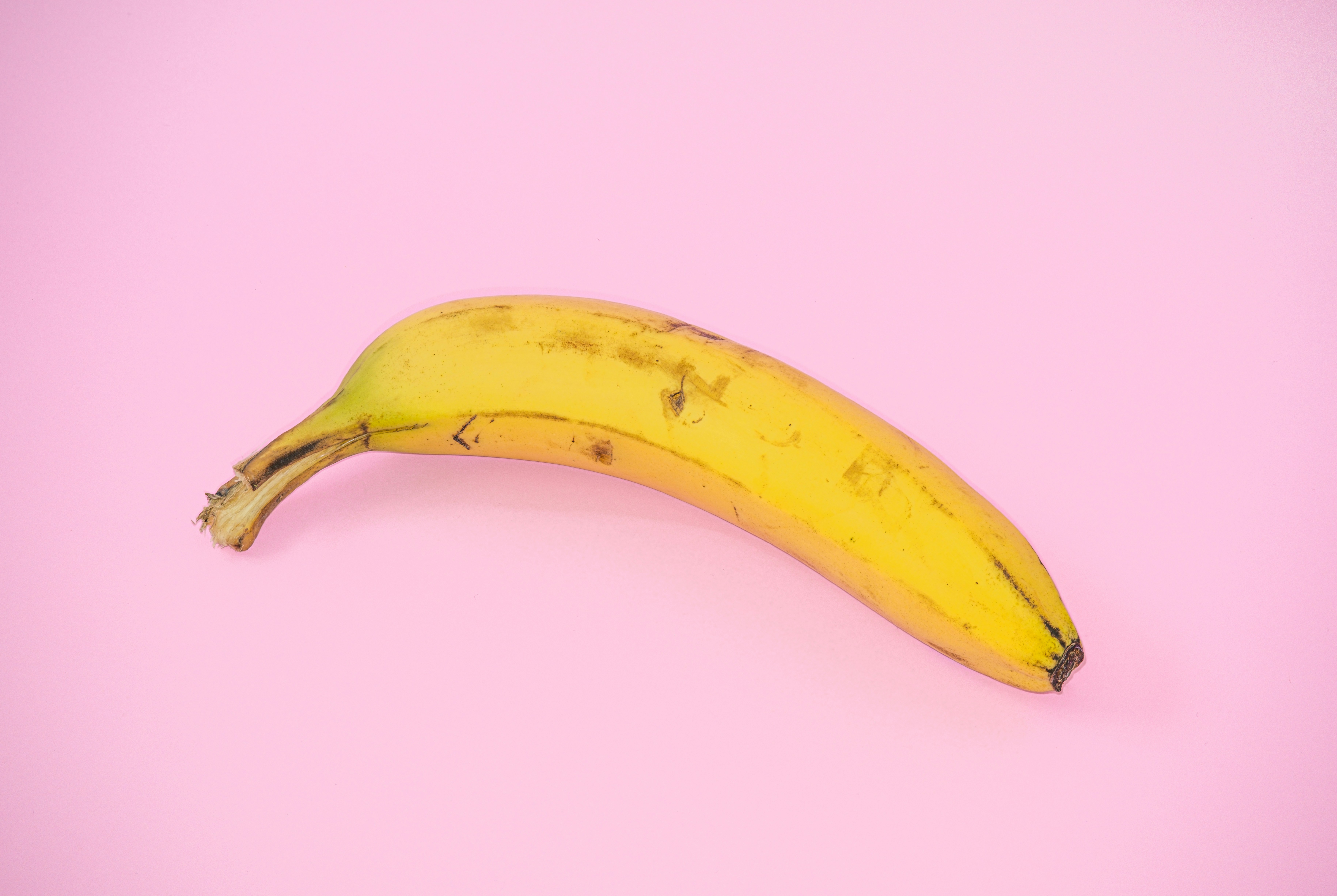 A ripe banana resting on a plain surface, showcasing its vibrant yellow peel and natural simplicity.