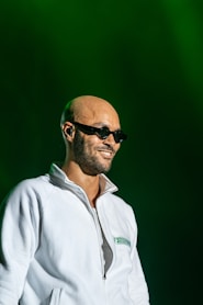 A bald man wearing sunglasses and a white jacket