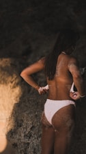 A woman in a white bikini standing next to a rock