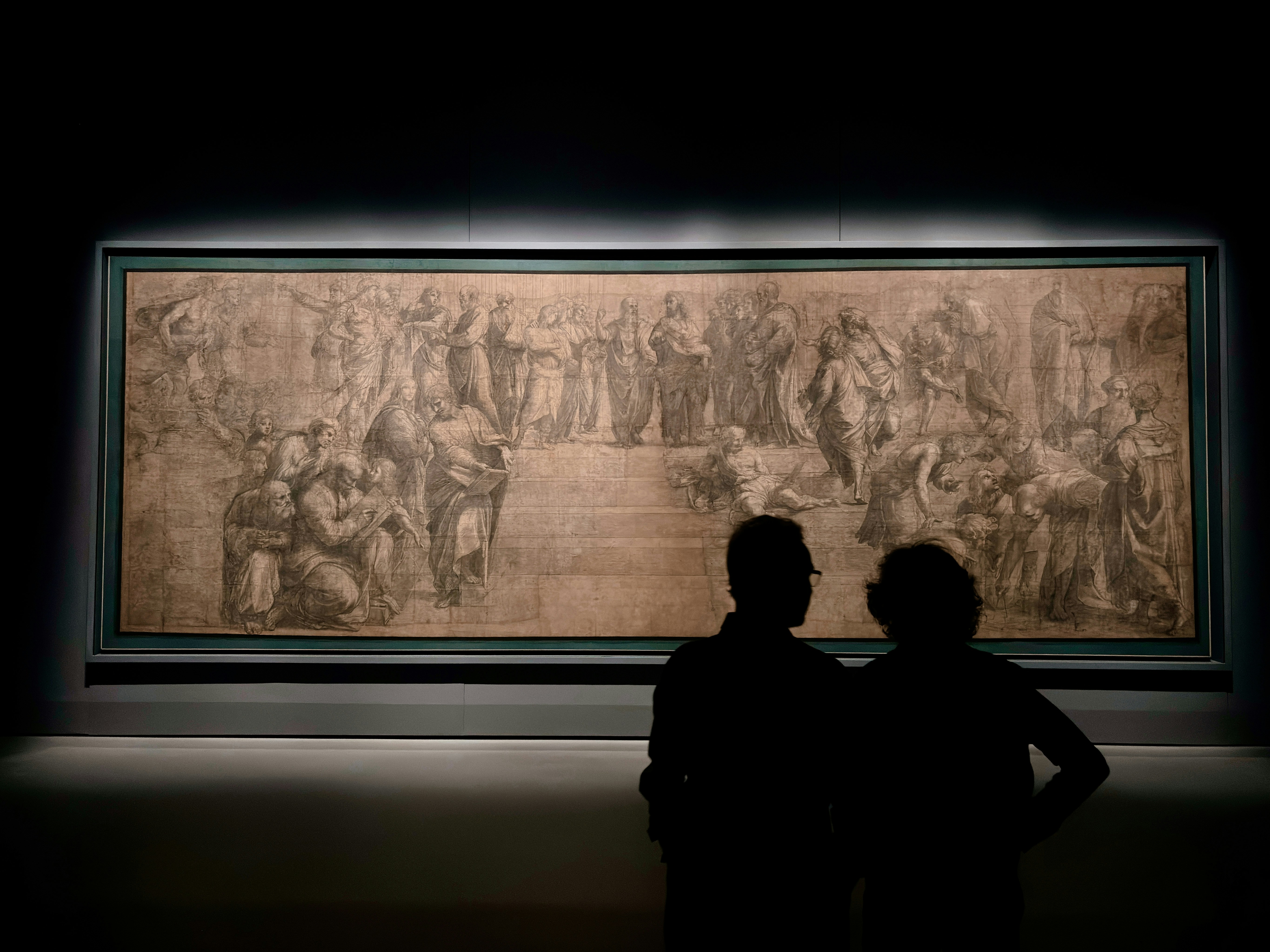 Two people standing in front of a painting in a dark room