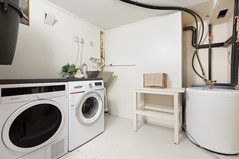 Modern laundry room with white washer and dryer, utility sink, water heater tank, and shelving