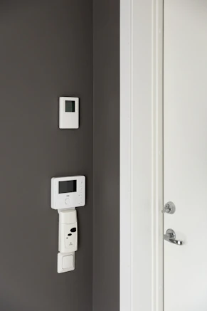 A bathroom with a toilet and a wall mounted thermostaer
