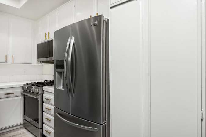 Stainless steel refrigerator in modern bright kitchen with white cabinets