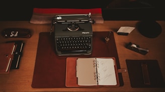 A desk with a typewriter, notebooks, and pen