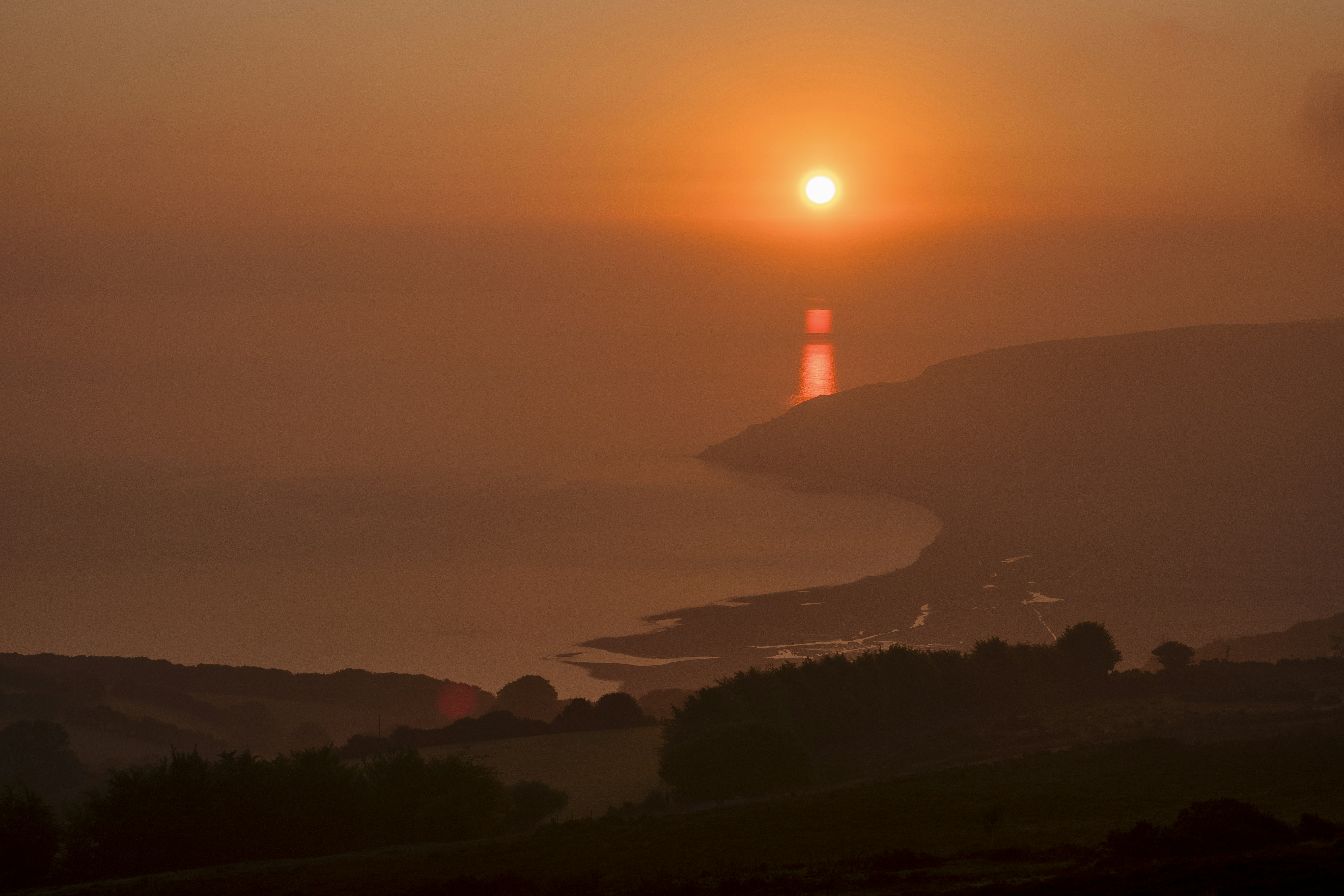 The sun is setting over the ocean with a lighthouse in the distance