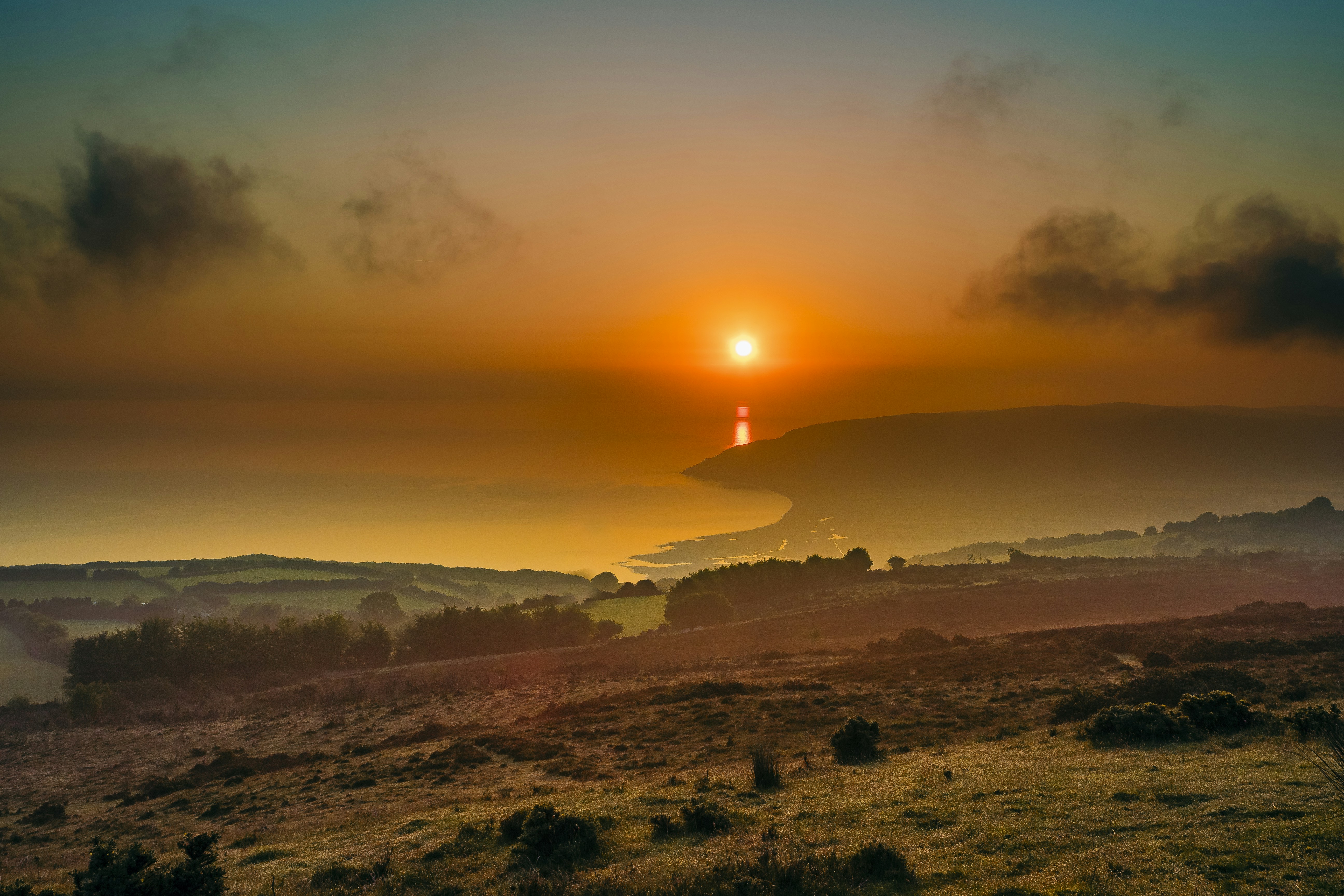 The sun is setting over a grassy hill