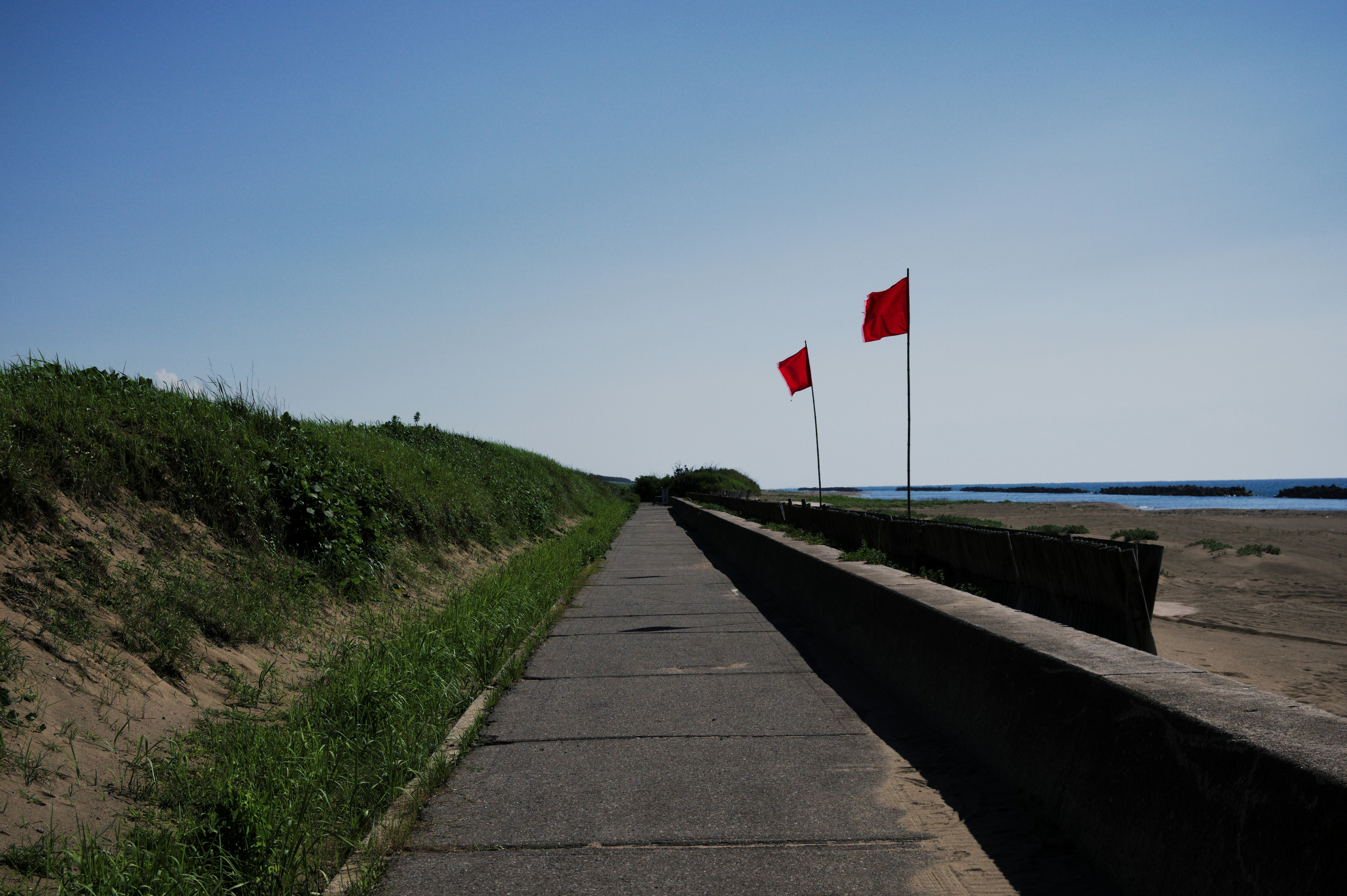 Two red flags on the side of a road next to the ocean photo – Free Road ...