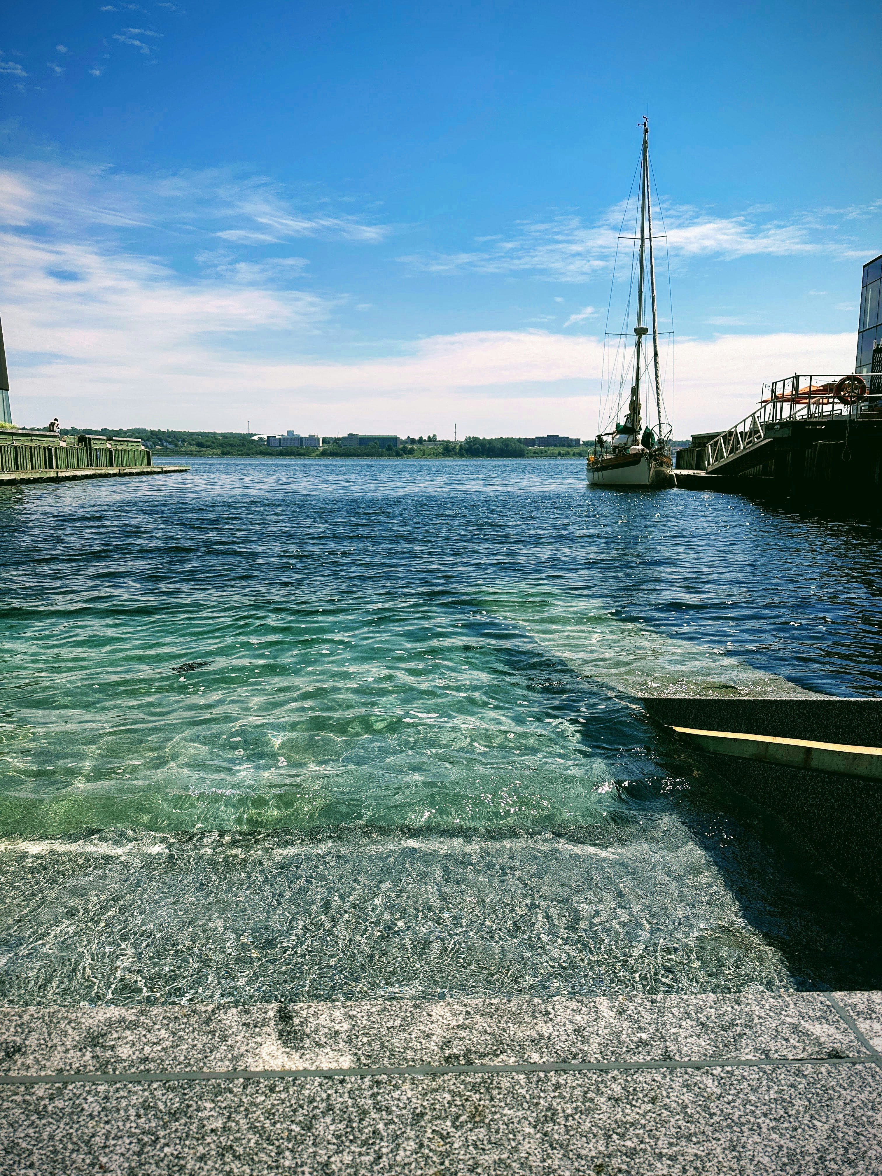 Sunlit coastal dock with navy rope and polished brass fittings, bright open sky, white sailboat in background