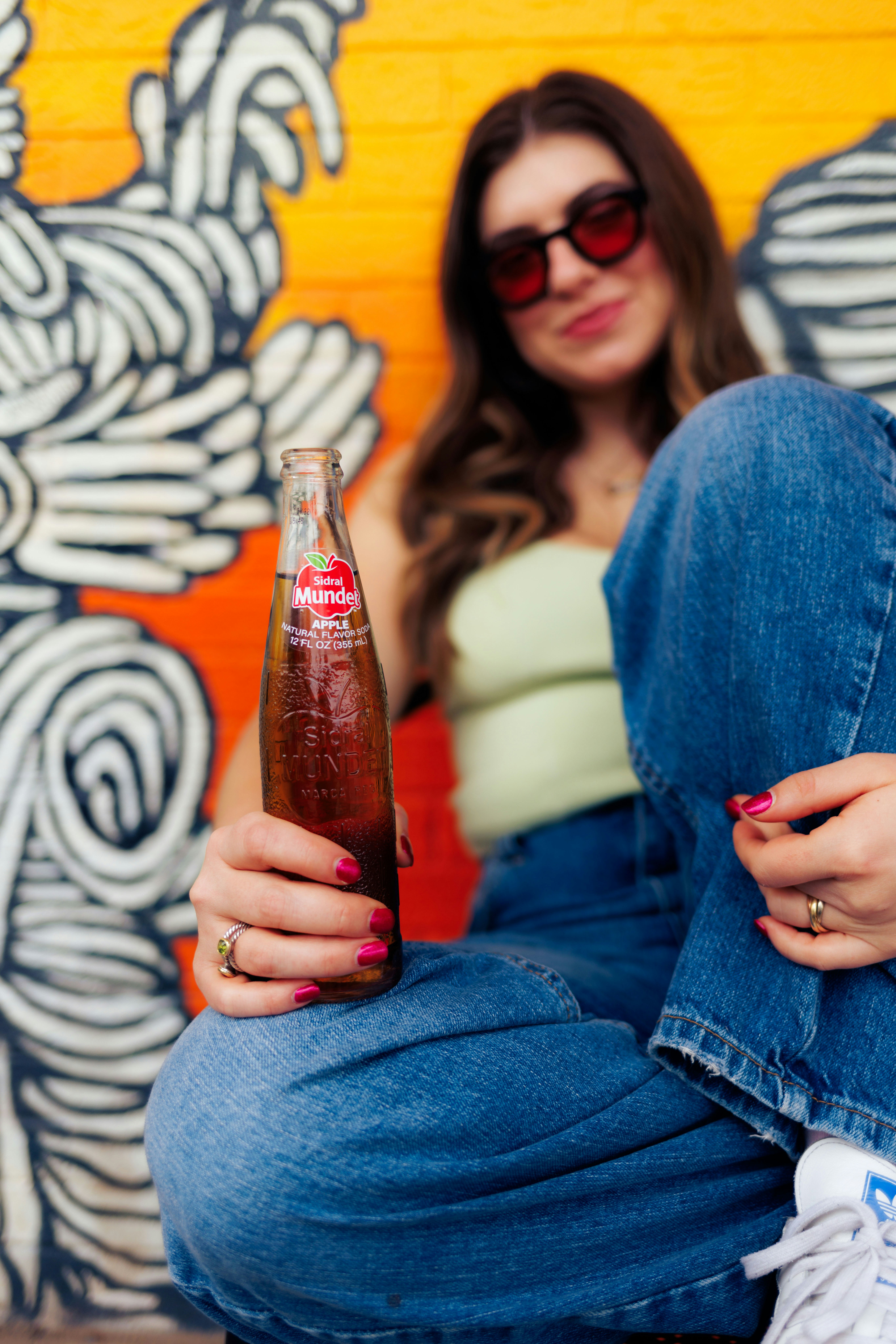 A woman sitting on the ground holding a bottle of soda