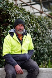 A man in a yellow jacket sitting on a cement wall