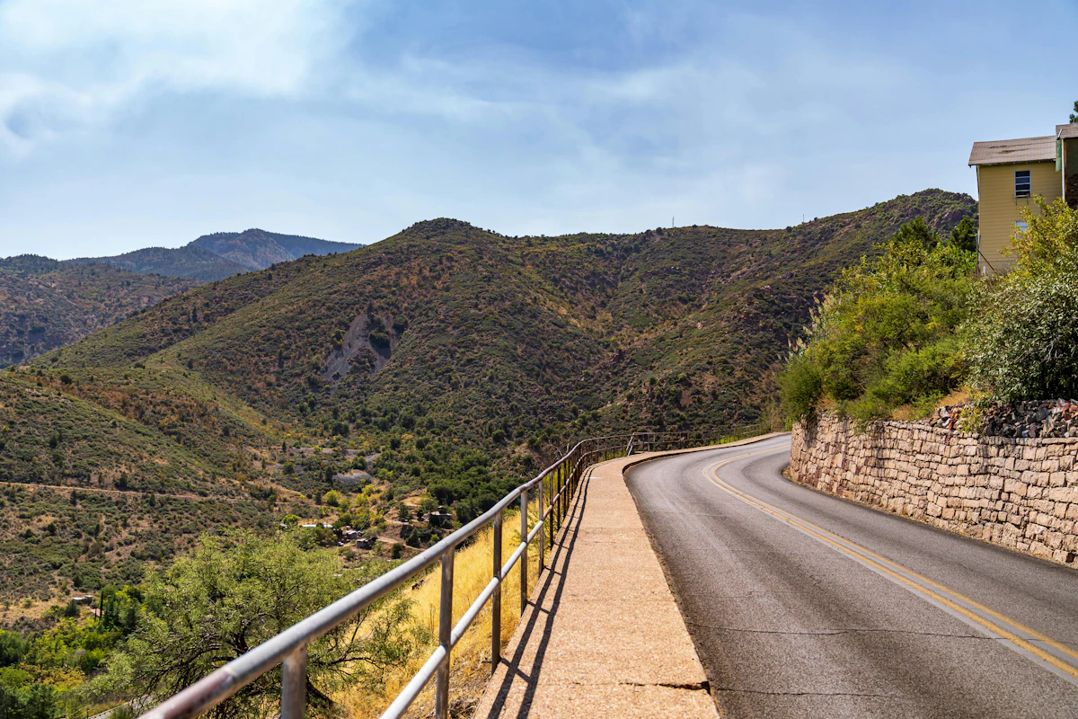 A road and sidewalk curving along a hillside in Jerome, with scrubby mountains behind