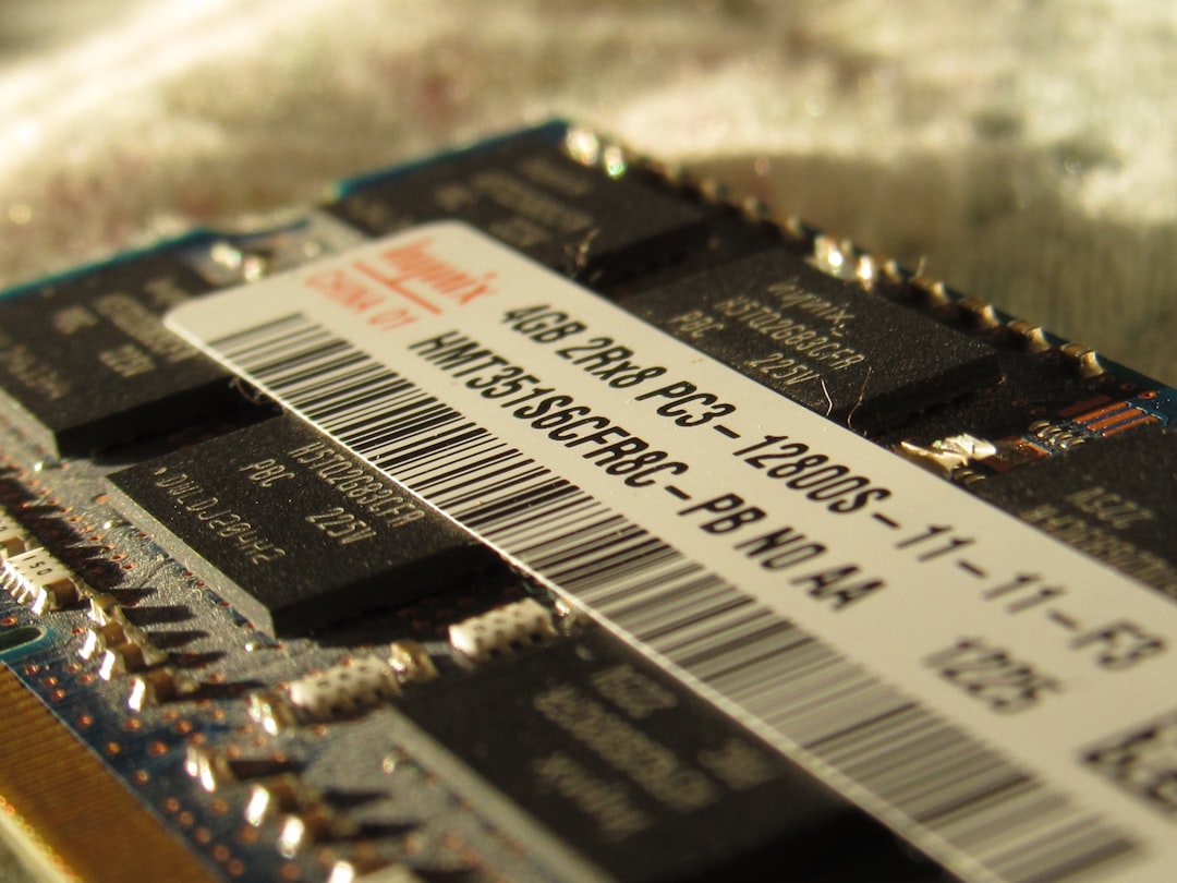 A close up of a computer memory chip, A close-up image of a laptop RAM module. The module is a small, rectangular circuit board with numerous gold-colored pins along its edges. Several black integrated circuits (ICs) are visible on the surface, along with text labels indicating specifications like "4GB 2Rx8 PC3-12800S-11-11-F3" and a barcode.