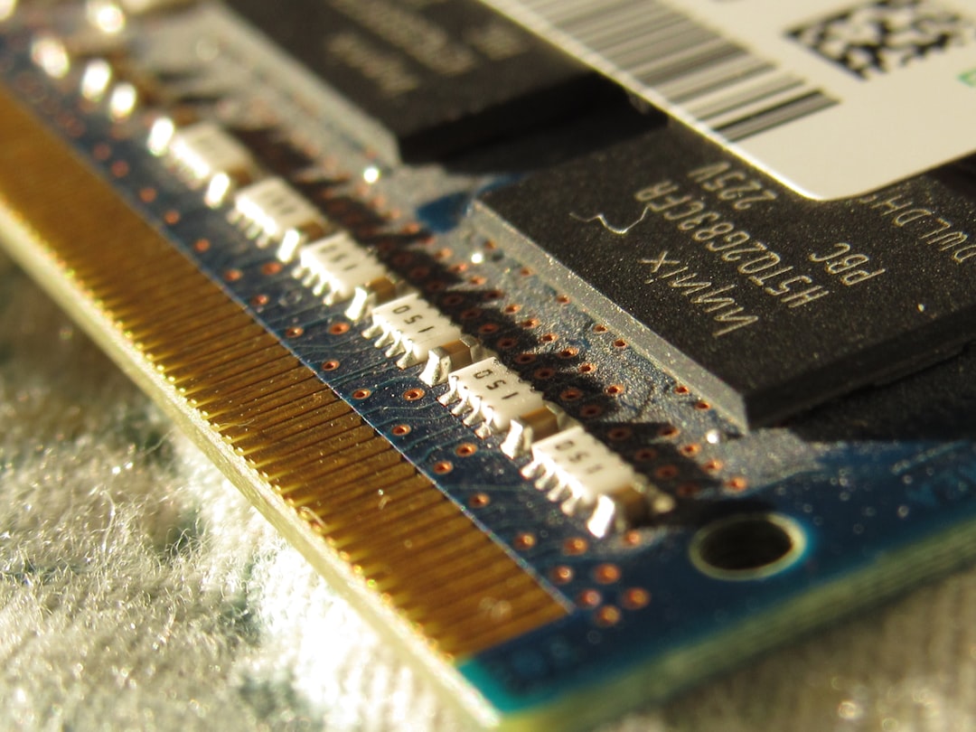A close up of a computer motherboard with a small chip, A close-up image of a laptop RAM module from a different angle. The module is a small, rectangular circuit board with numerous gold-colored pins along its edges. Several black integrated circuits (ICs) are visible on the surface, with text labels indicating specifications like "HSTO2683CFR" and "225V". The module also features a sticker containing a barcode and the text "Hynix PBC".
