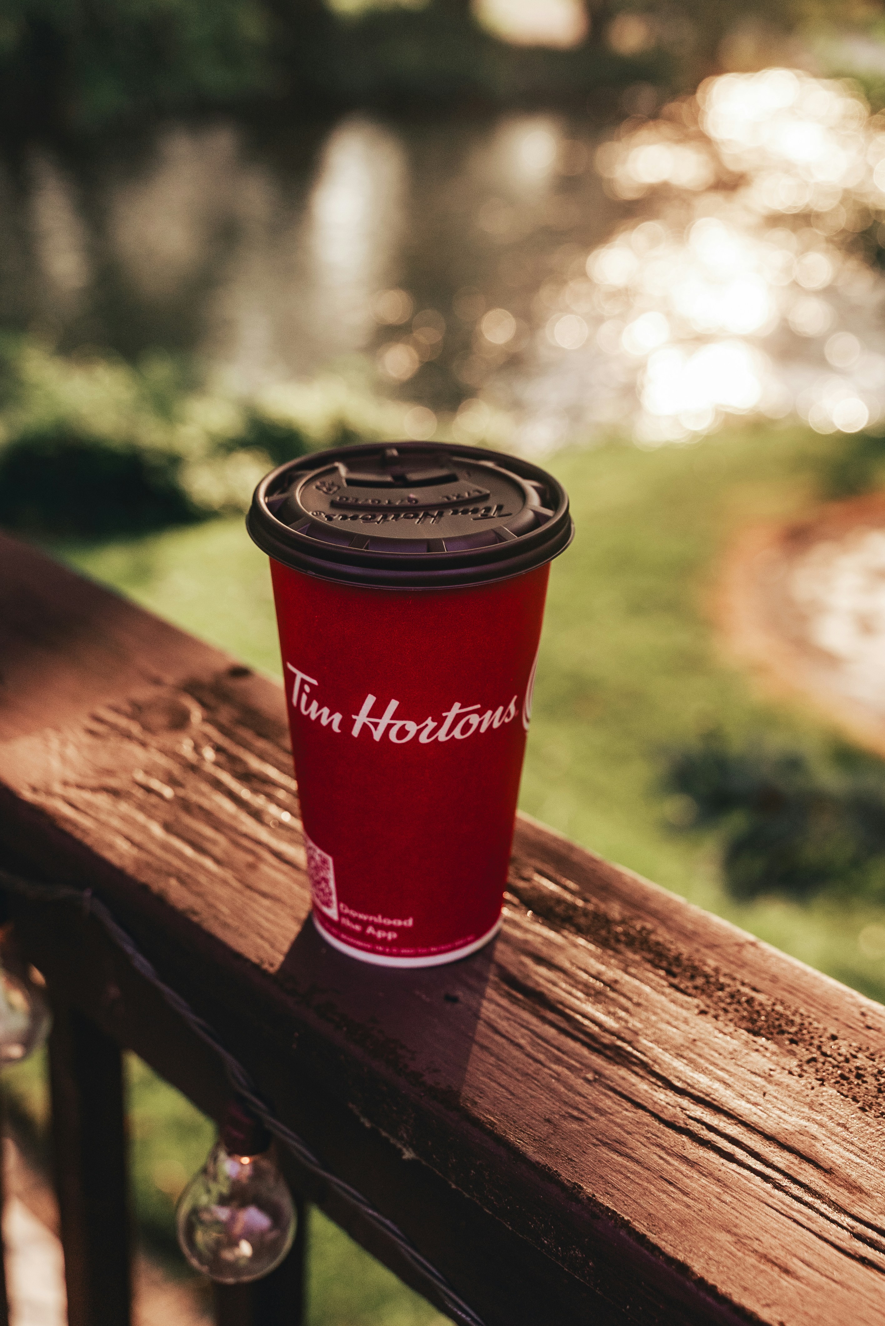 Secangkir kopi merah duduk di atas pagar kayu