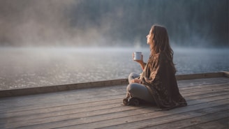 A woman sitting on a dock holding a cup of coffee