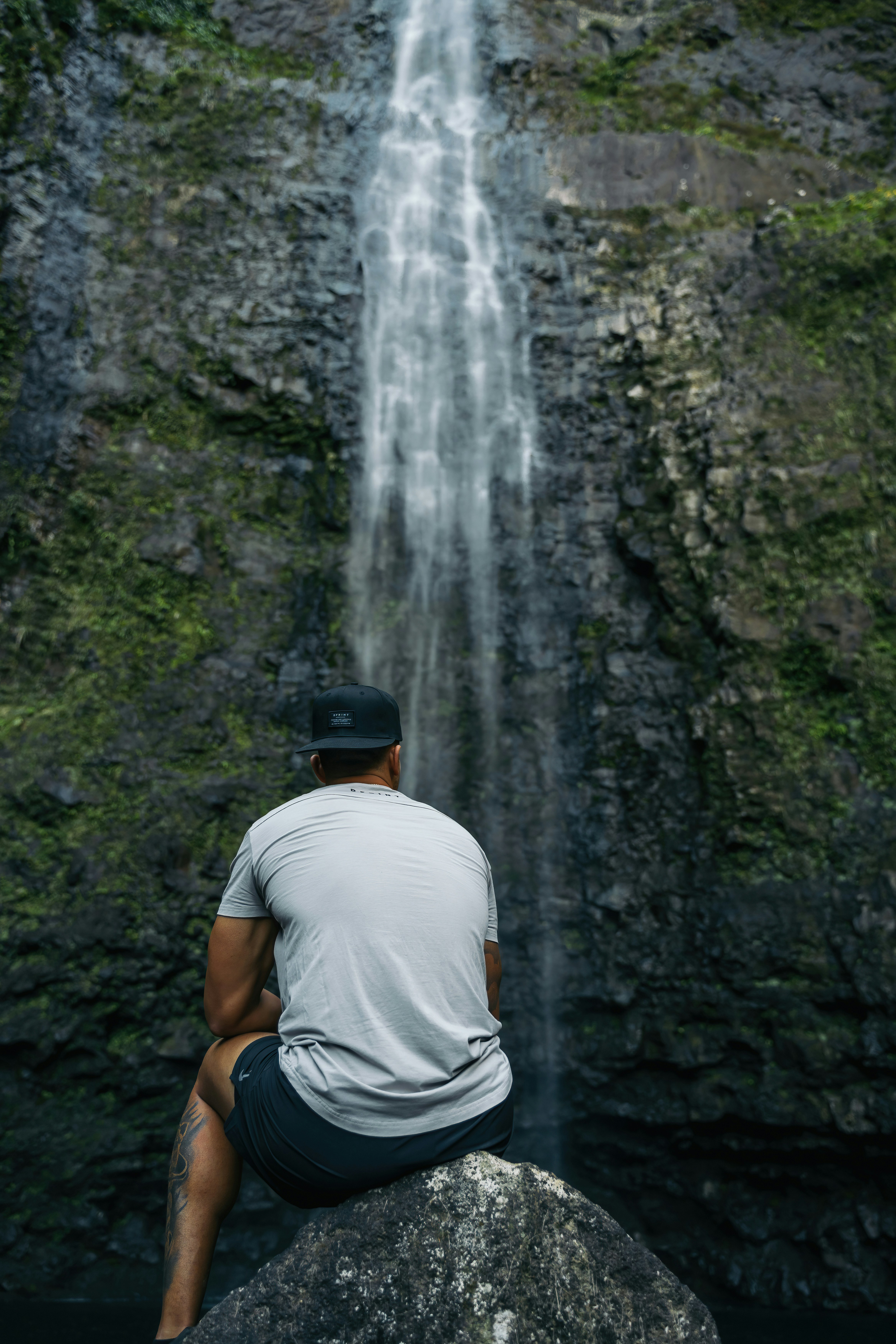 A man sitting on a rock in front of a waterfall