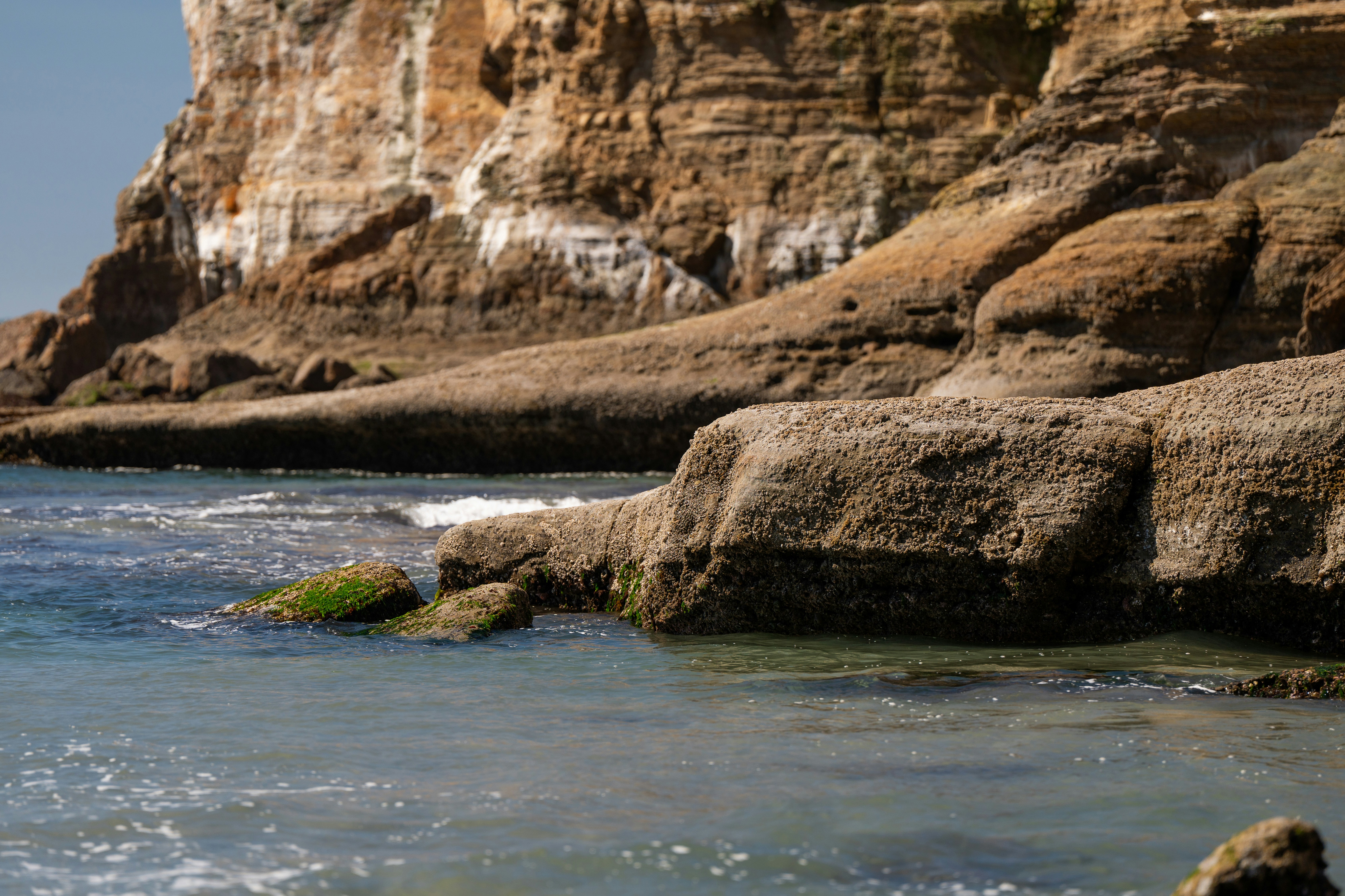 A rocky beach with clear blue water and a cliff in the background