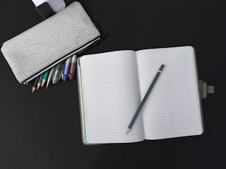 An open notebook with a pen and pencil on a table