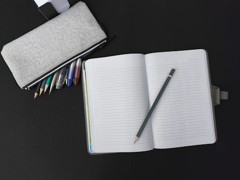 An open notebook with a pen and pencil on a table