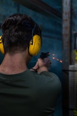 A man wearing yellow ear muffs while holding a gun