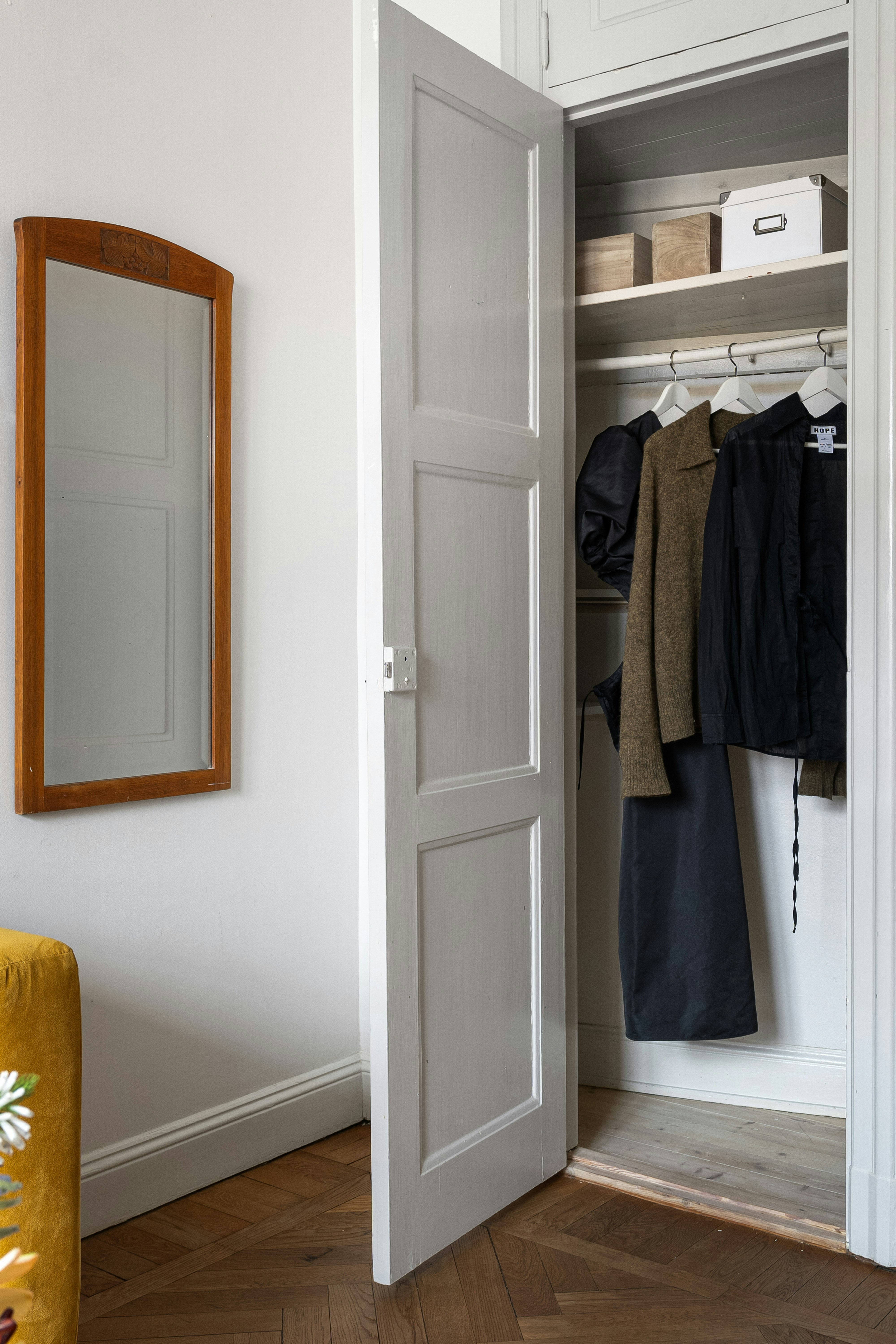 A white closet with a mirror and coat rack