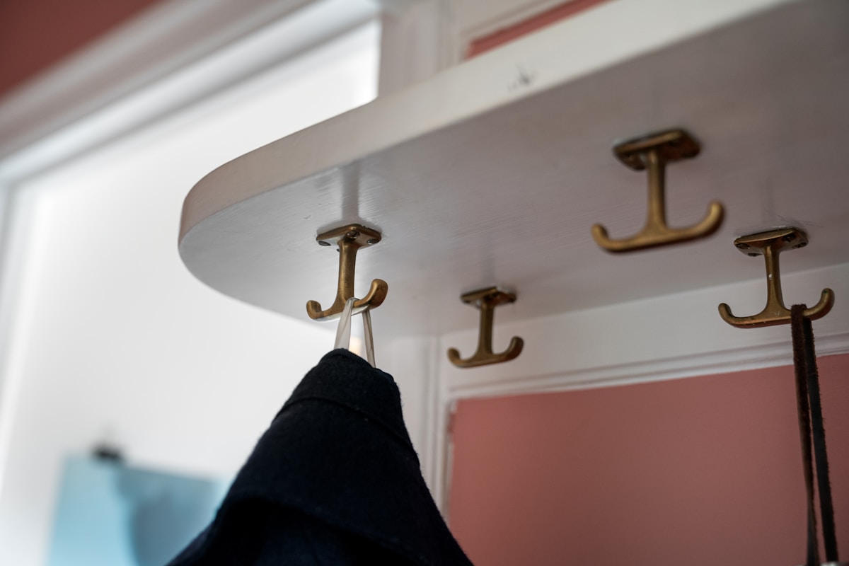 Close-up of brass coat hooks mounted under a white floating shelf above door height
