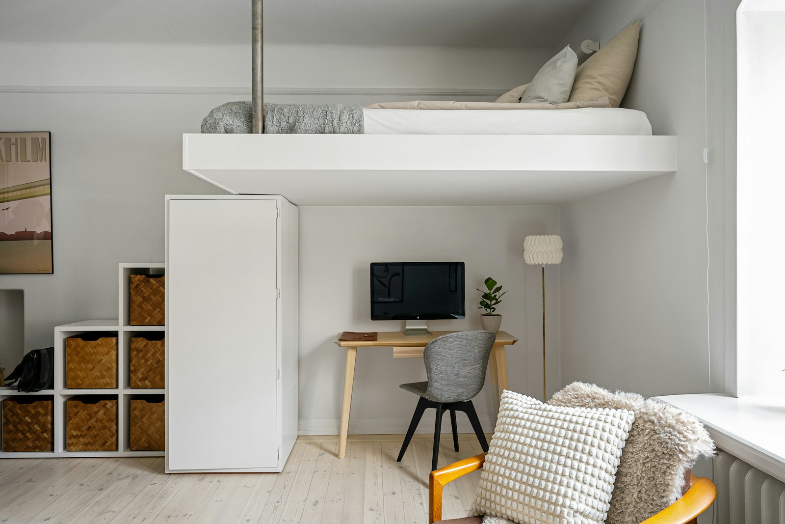 A studio room where a loft bed sits above a working desk, letting one space hold sleeping and working