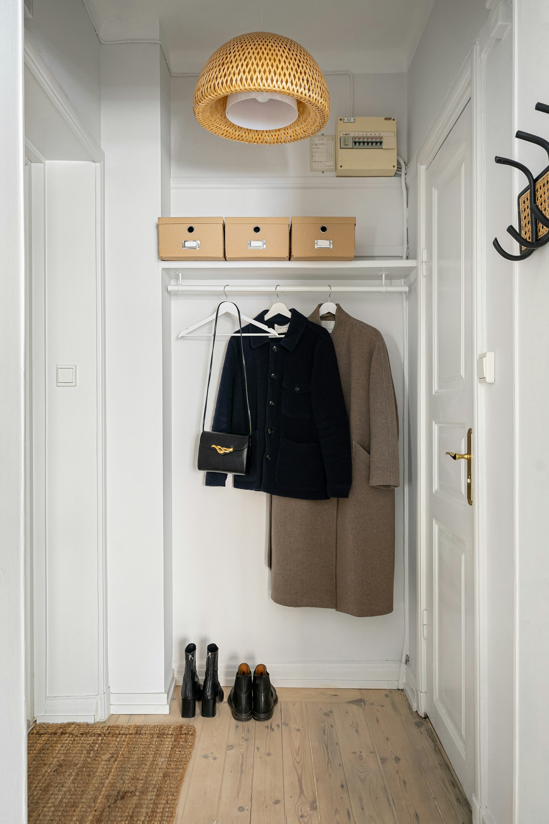 A closet with a coat and shoes on the floor