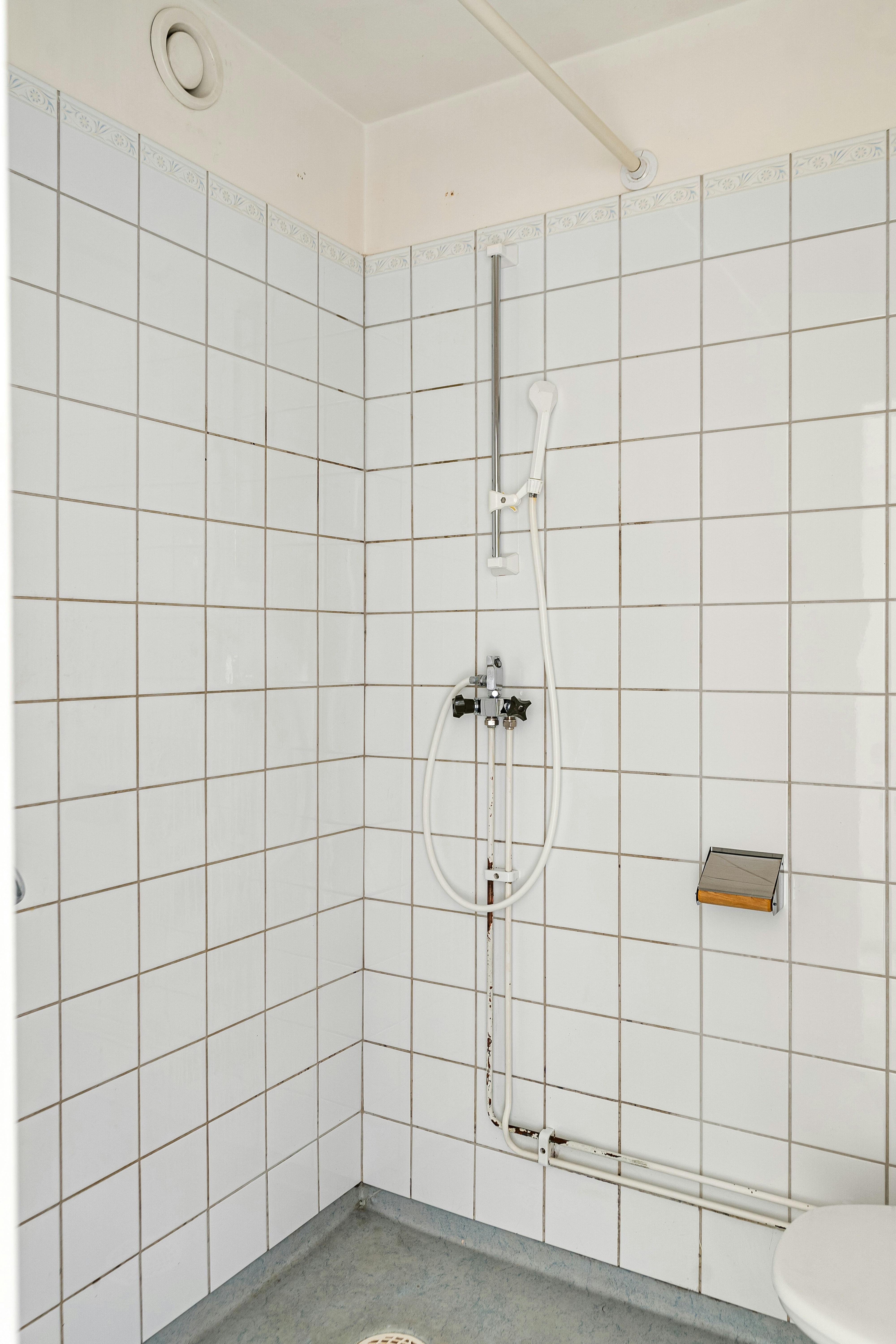 A white tiled bathroom with a shower and toilet