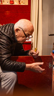 An old man sitting at a table with a cigarette in his mouth
